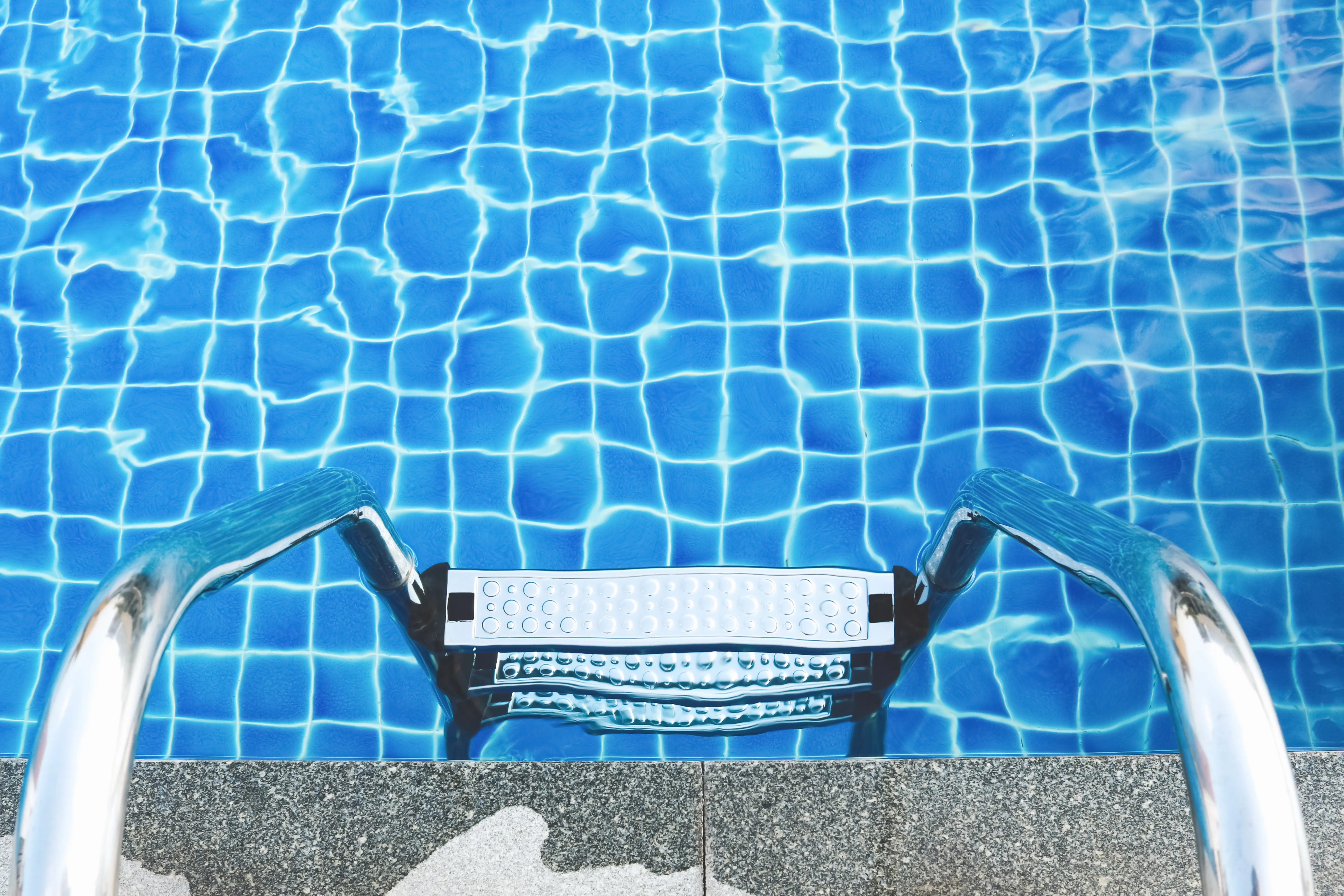 Escalera metálica bajando a una piscina de agua azul vista desde arriba.